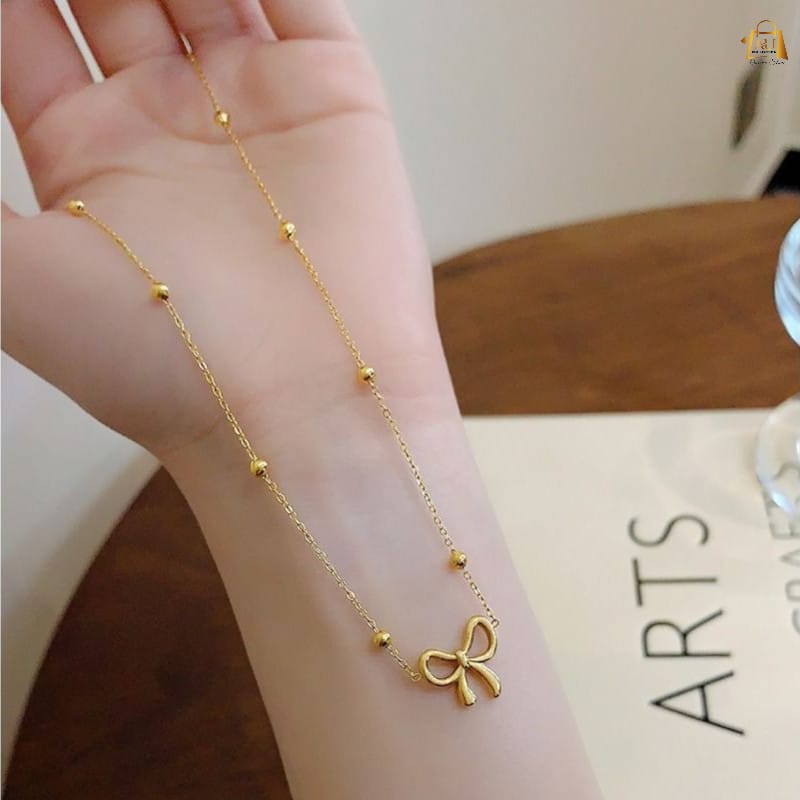 Gold bracelet with a bow charm on a person's wrist against a neutral background