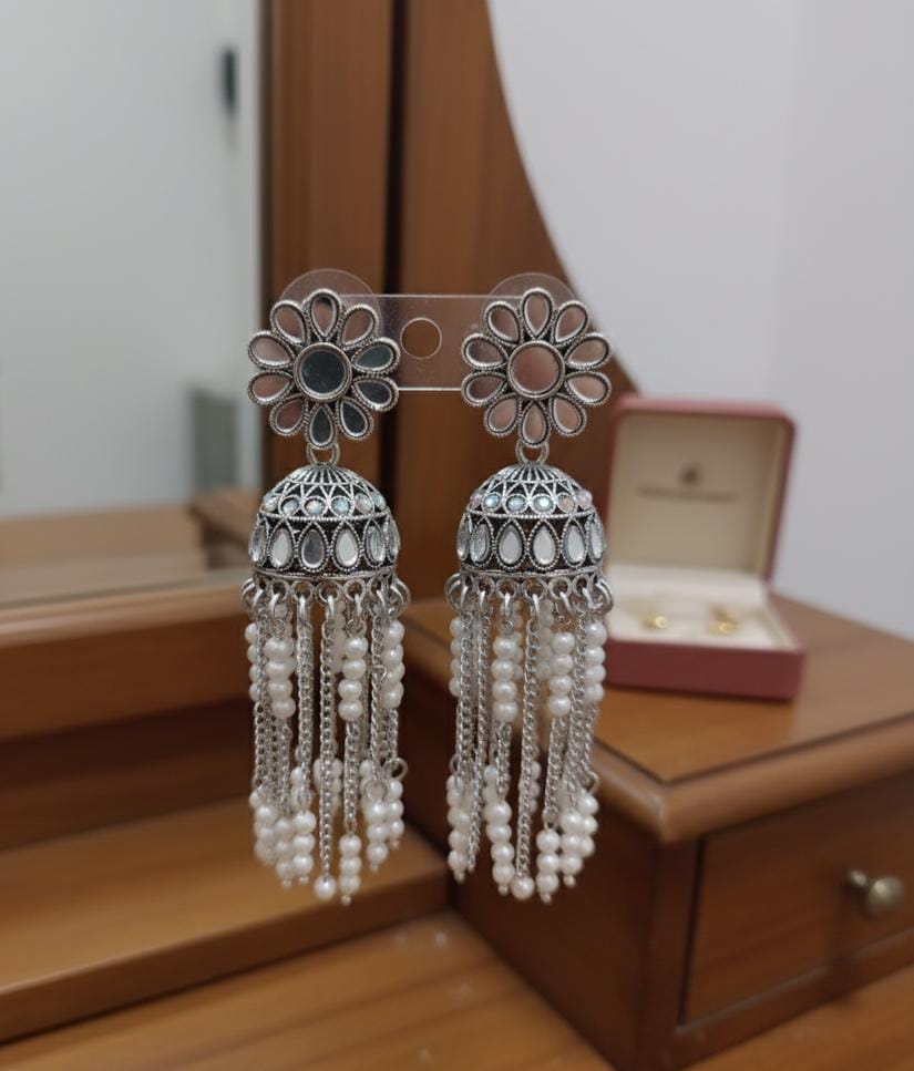 Pair of silver earrings with floral designs and pearl-like beads on a wooden surface.