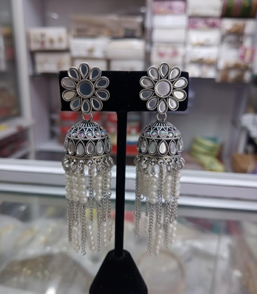Pair of silver floral earrings with dangling chains on a black stand.