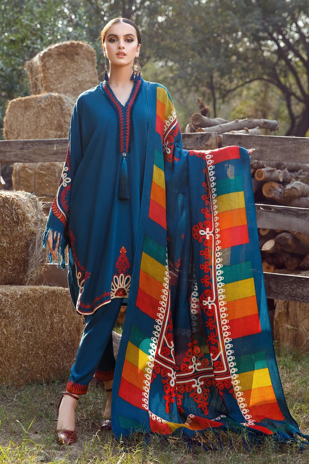 Woman holding a colorful traditional scarf with a blue dress in an outdoor setting.