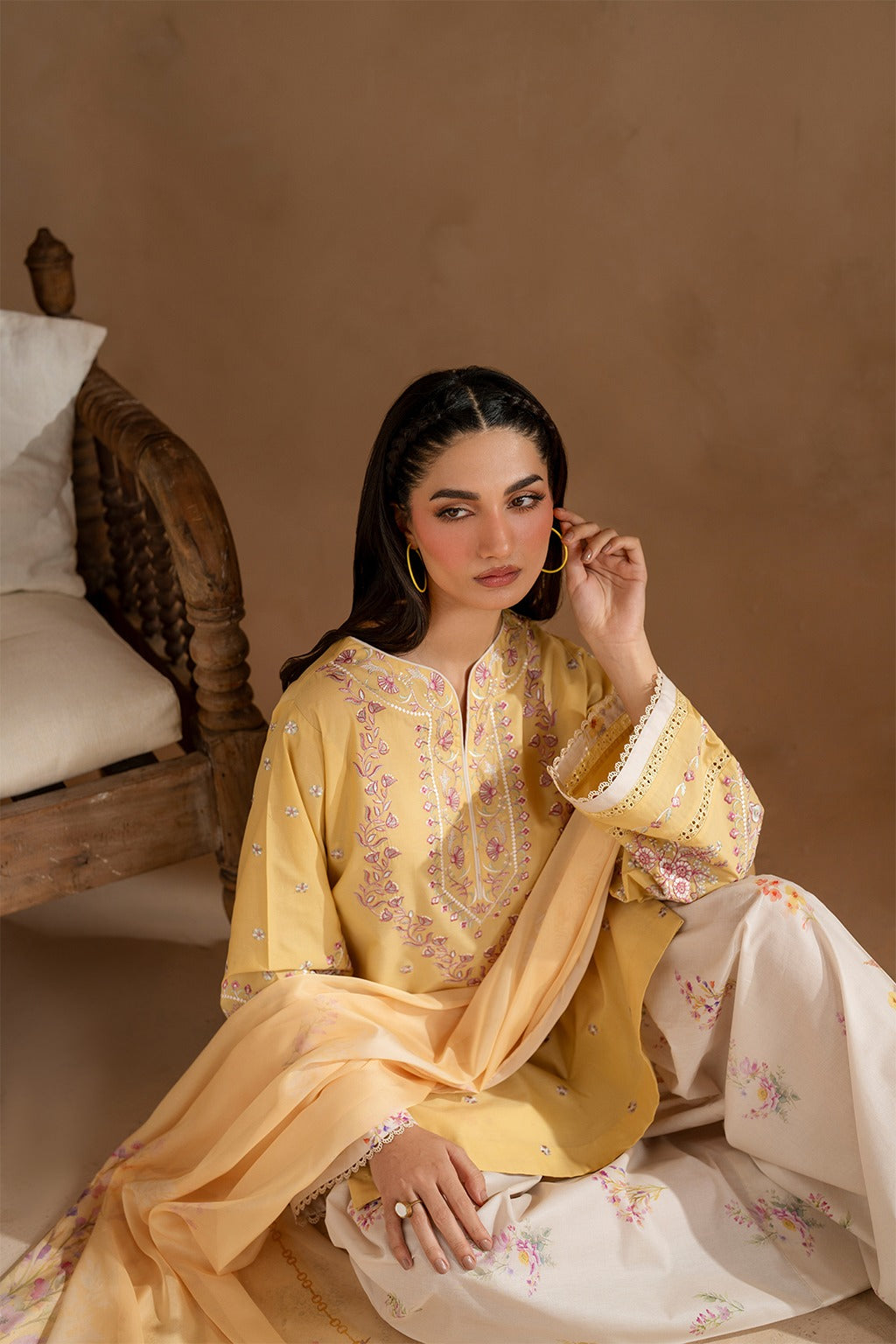 Woman in a yellow embroidered traditional outfit sitting on a wooden chair.