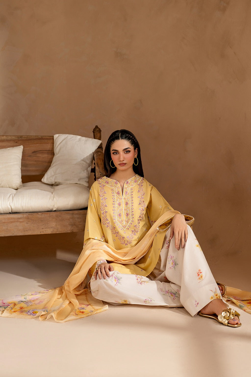 Woman in traditional outfit sitting on a bed with a neutral background