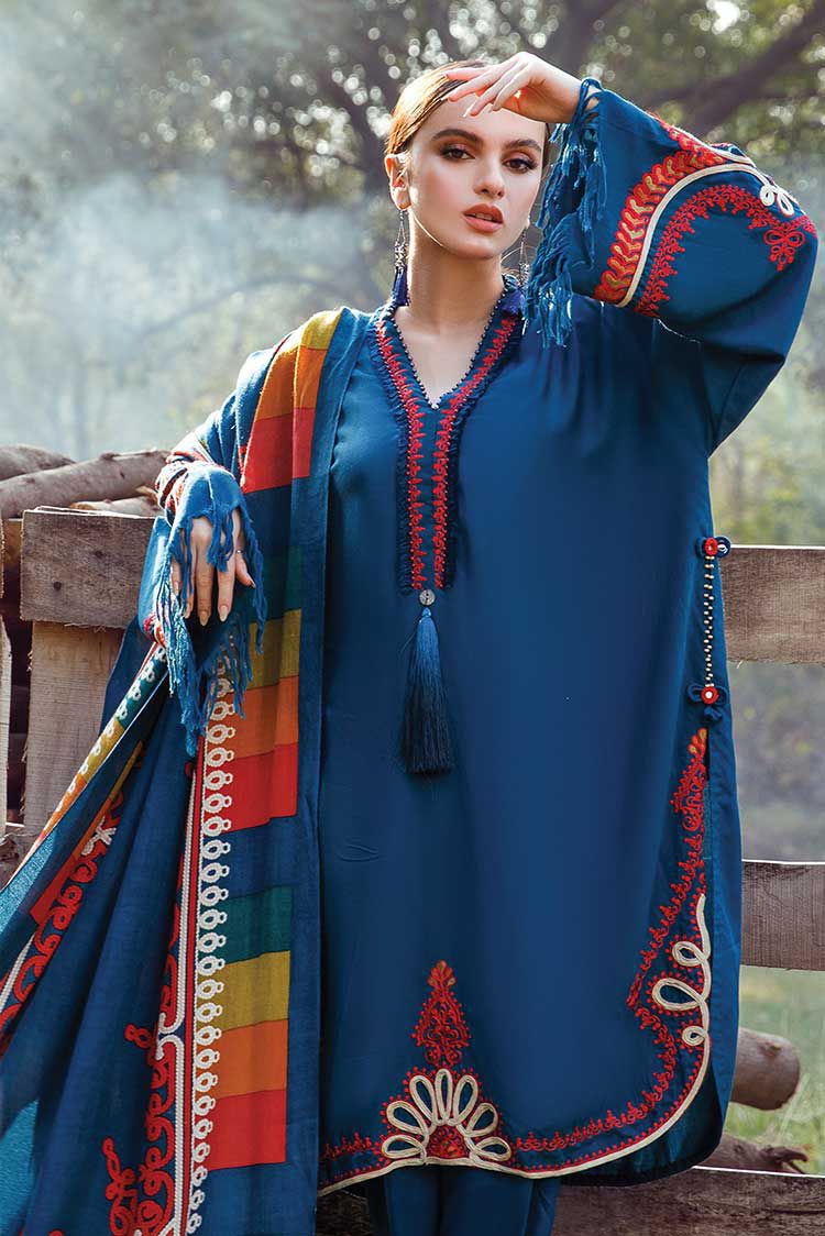 Woman wearing a blue embroidered dress with colorful patterns outdoors.