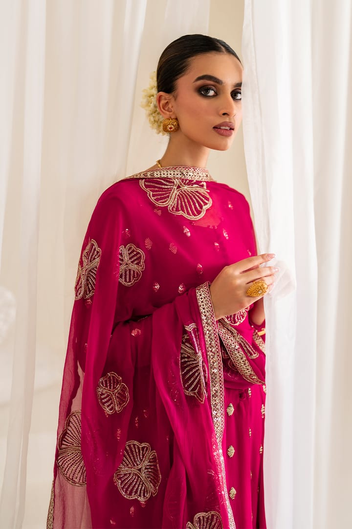 Woman wearing a pink traditional outfit with gold embroidery against a white curtain background
