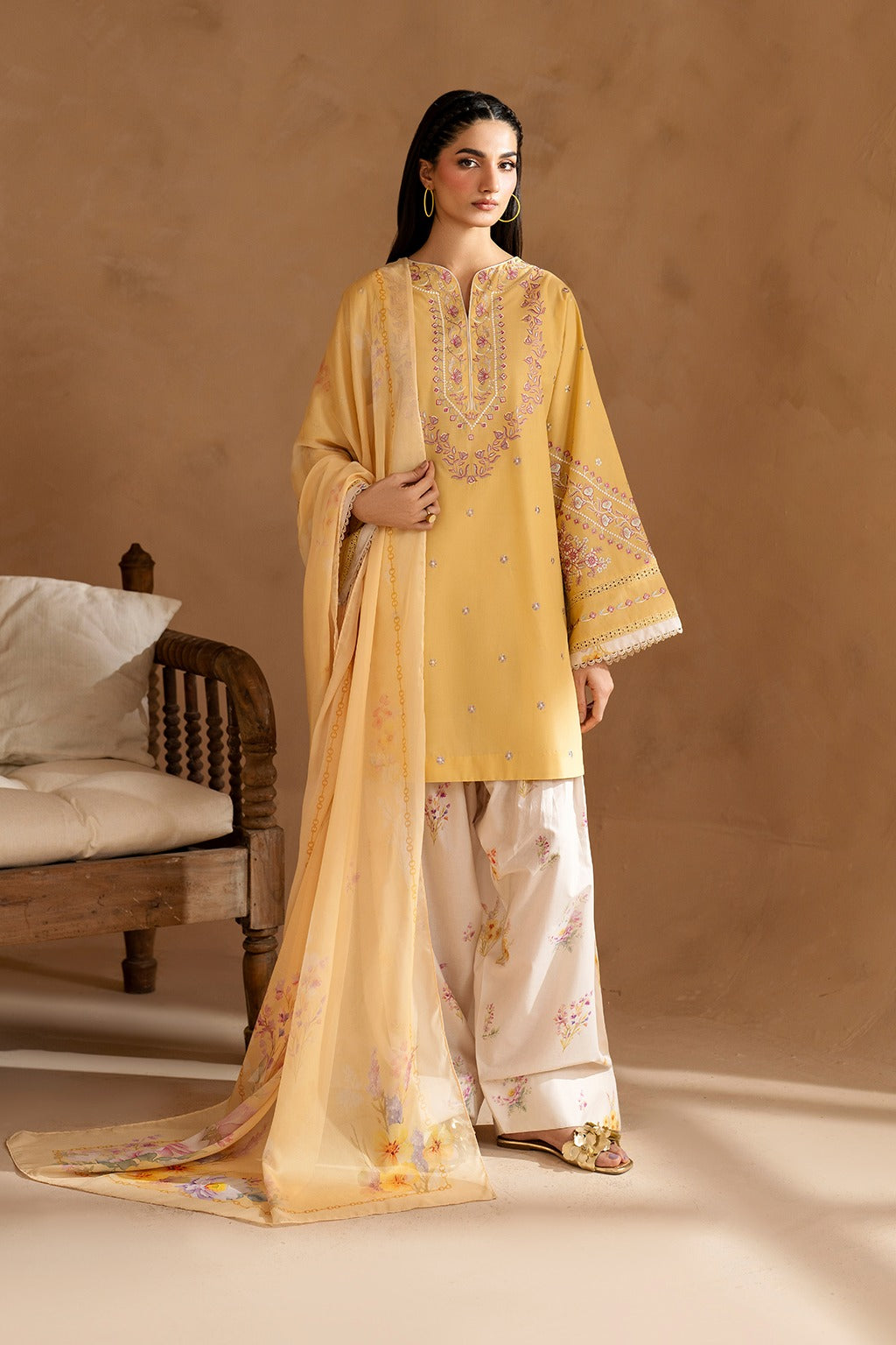 Woman wearing a traditional outfit with a yellow top and white pants against a beige background