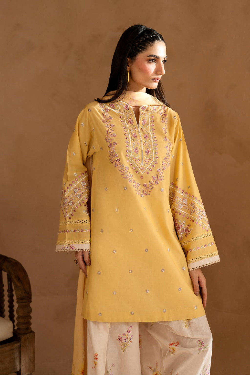 Woman wearing a yellow embroidered kurta with white pants against a brown background